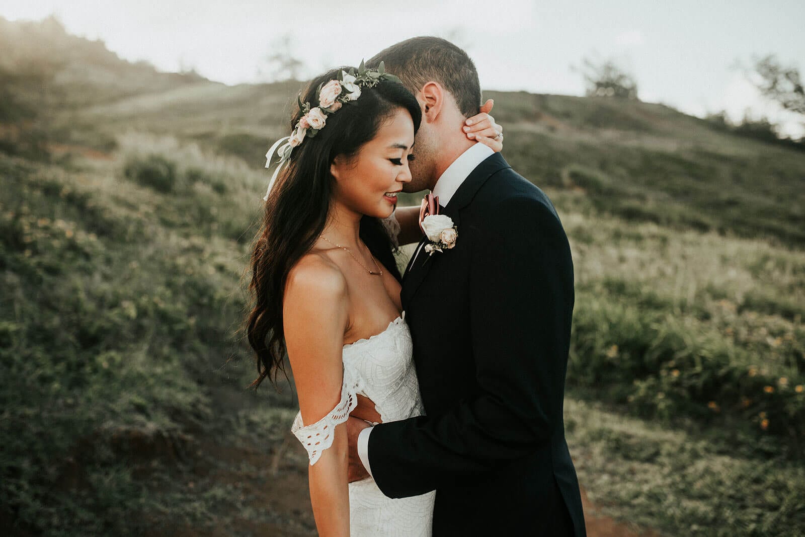 Brunette bride wearing Grace Loves Lace Paloma Gown embracing groom on grassy hill