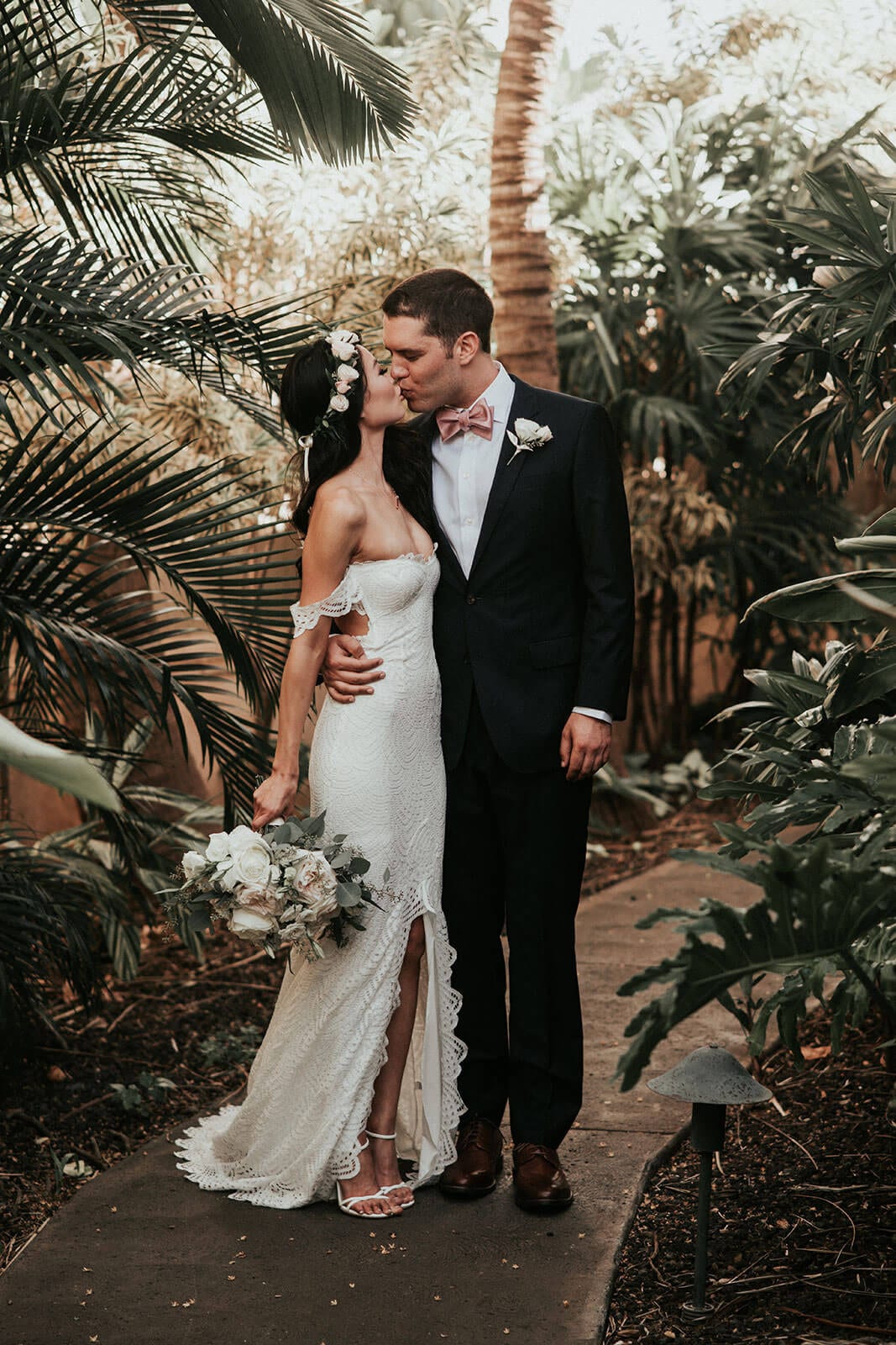 Brunette bride wearing Grace Loves Lace Paloma Gown kissing groom on garden path