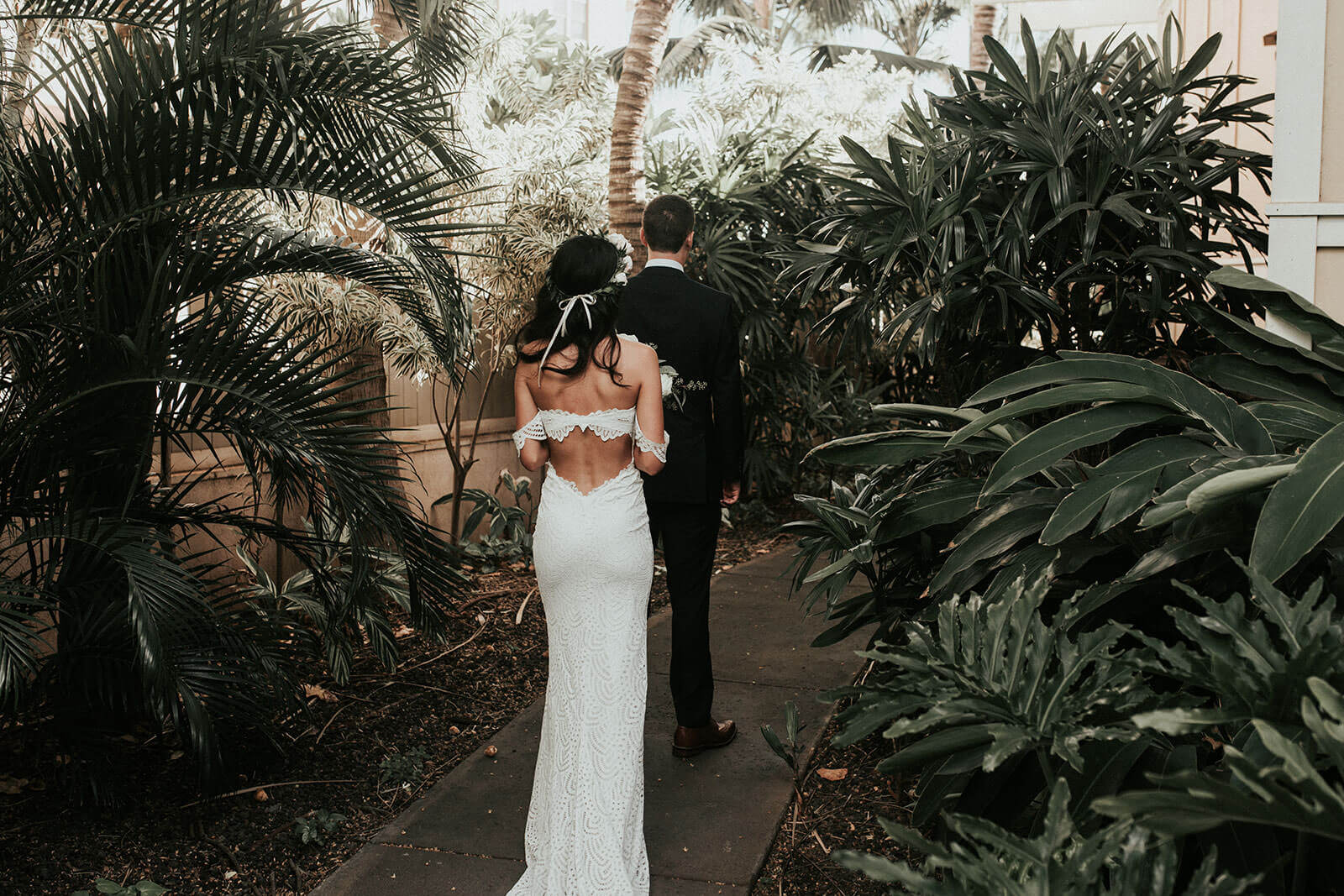 Back shot of bride wearing Grace Loves Lace Paloma Gown walking behind groom along garden path