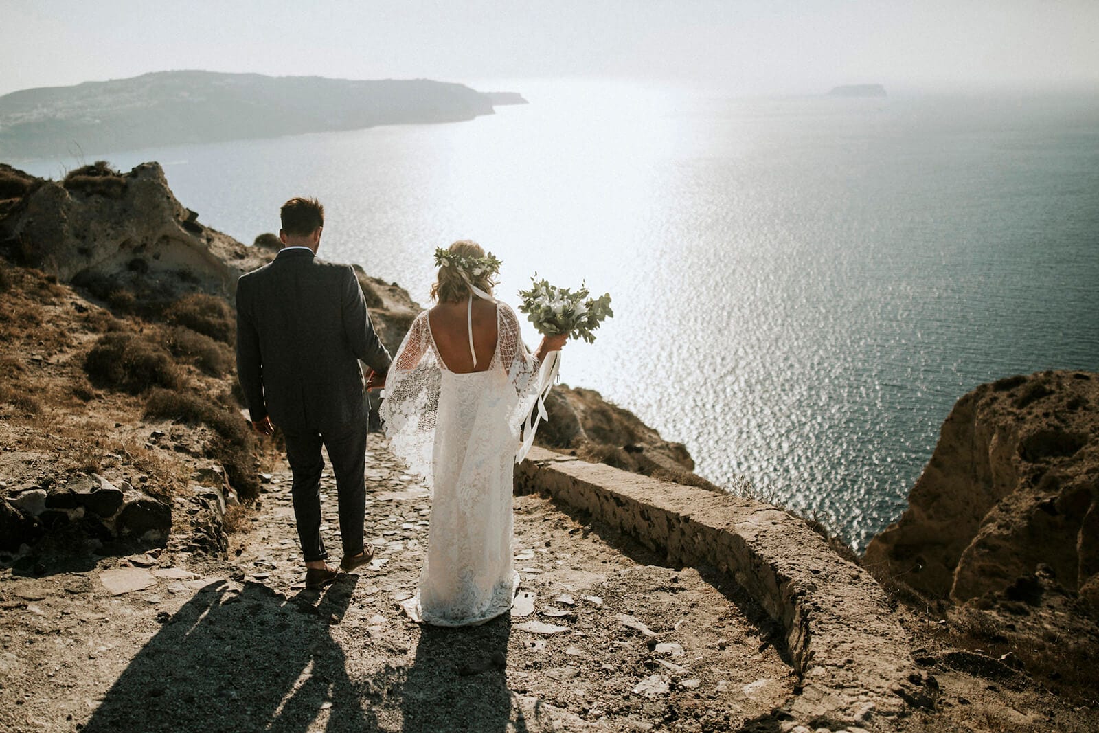 Bride wearing Grace Loves Lace Verdelle 2.0 Gown holding hands with groom on seaside cliff