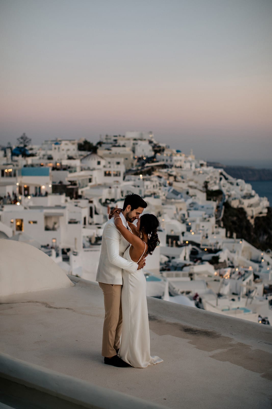 Brunette bride wearing Grace Loves Lace Arlo Gown embracing groom behind cityscape