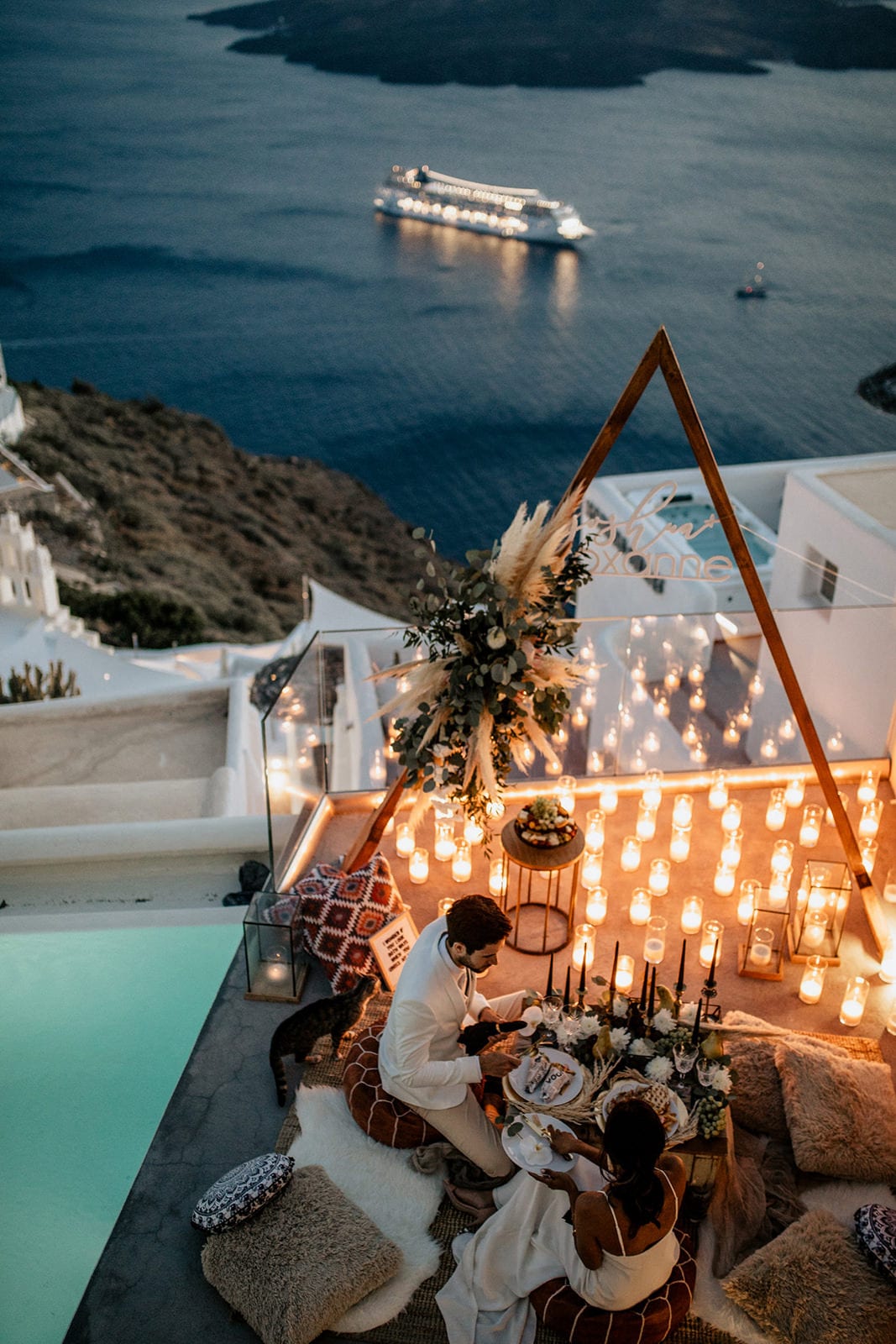 Brunette bride wearing Grace Loves Lace Arlo Gown sitting with groom in romantic candlelit setting by ocean