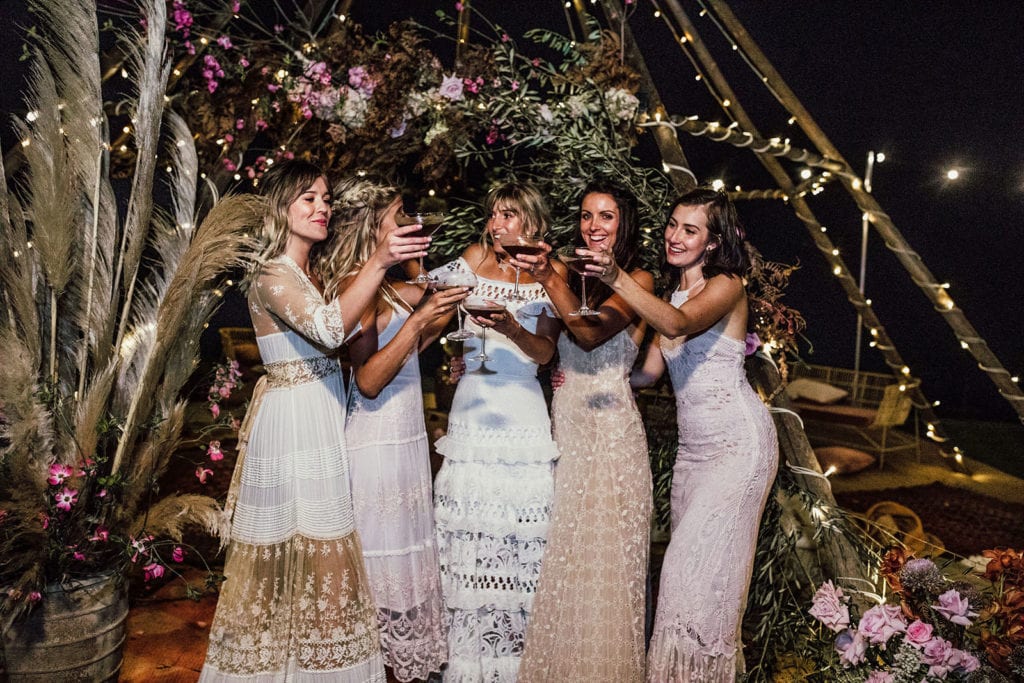 Blonde bride wearing Grace Loves Lace Coco Gown with bridesmaids holding wine glasses